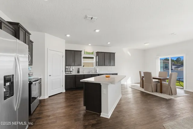 a large kitchen with stainless steel appliances kitchen island granite countertop a large refrigerator a sink a stove and oven with wooden floor