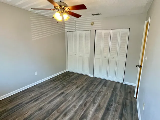 a view of an empty room with wooden floor and a ceiling fan