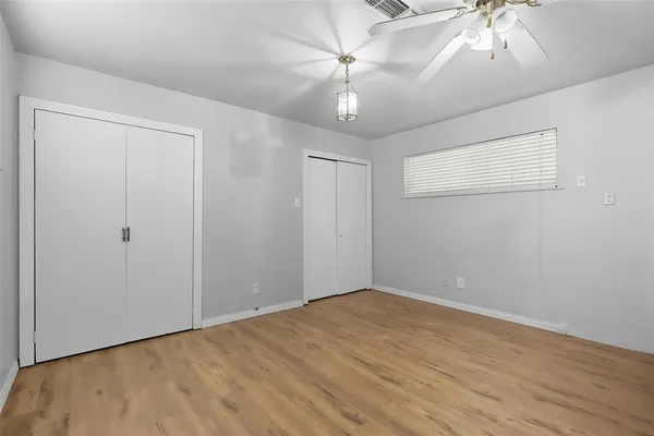 an empty room with a chandelier fan and wooden floor