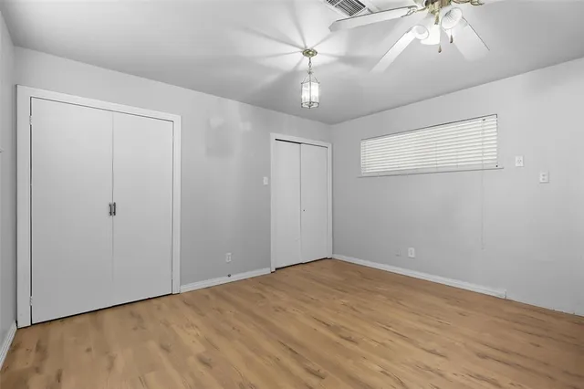 an empty room with a chandelier fan and wooden floor