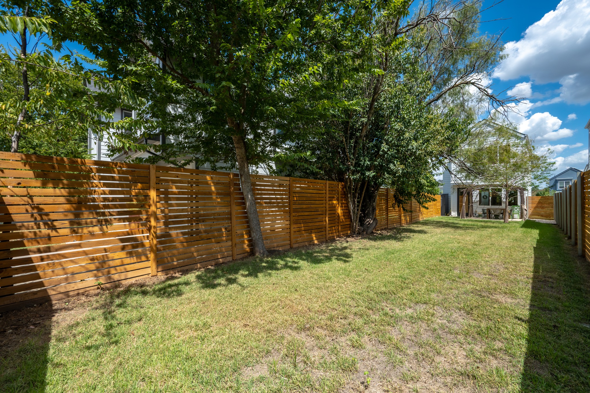 1190 Sarabeth Way Austin, TX 78721 - Photo 20 of 22 Lush mature trees shade a grassy lawn enclosed by modern wooden horizontal fencing.