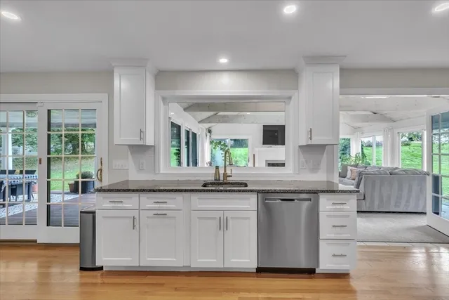 a kitchen with granite countertop a stove a sink and white cabinets with wooden floor