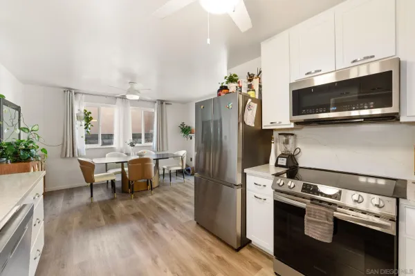 a kitchen with stainless steel appliances a stove a microwave a refrigerator a stove and white cabinets with wooden floor