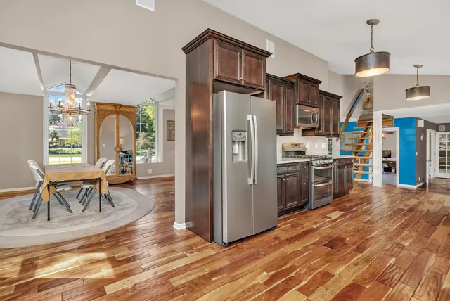 a kitchen with stainless steel appliances granite countertop a refrigerator a stove and a dining table with wooden floor