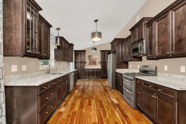 a large kitchen with stainless steel appliances granite countertop a stove a sink dishwasher and wooden cabinets with wooden floor