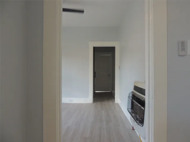 a view of a kitchen from an empty room with wooden floor and a fireplace