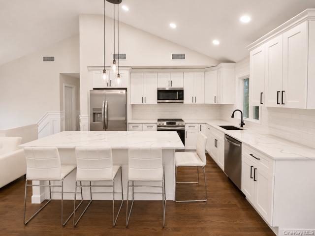 321 Sherbrooke Road Lindenhurst, NY 11757 - Photo 8 of 21 Modern kitchen featuring white shaker-style cabinetry, quartz countertops, stainless steel appliances including a gas range and built-in microwave, and a large center island with seating