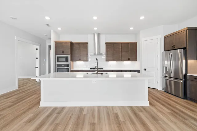 a large kitchen with stainless steel appliances a large counter top a stove and a refrigerator