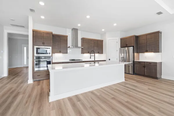 a large kitchen with stainless steel appliances kitchen island a large counter top and wooden floors