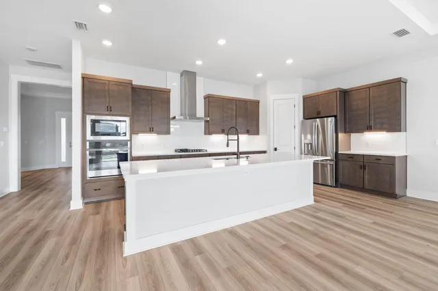 a large kitchen with stainless steel appliances kitchen island a large counter top and wooden floors