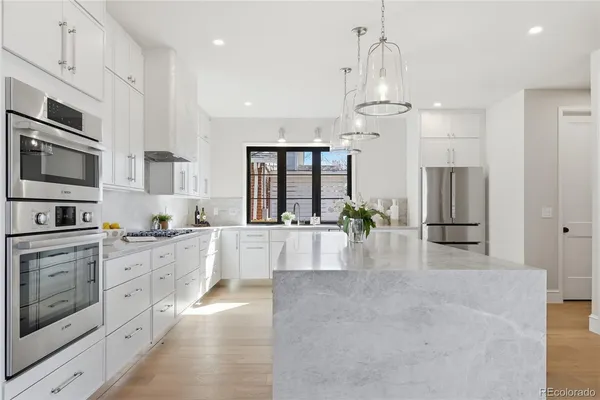 a large white kitchen with kitchen island granite countertop lots of counter space a refrigerator and cabinets