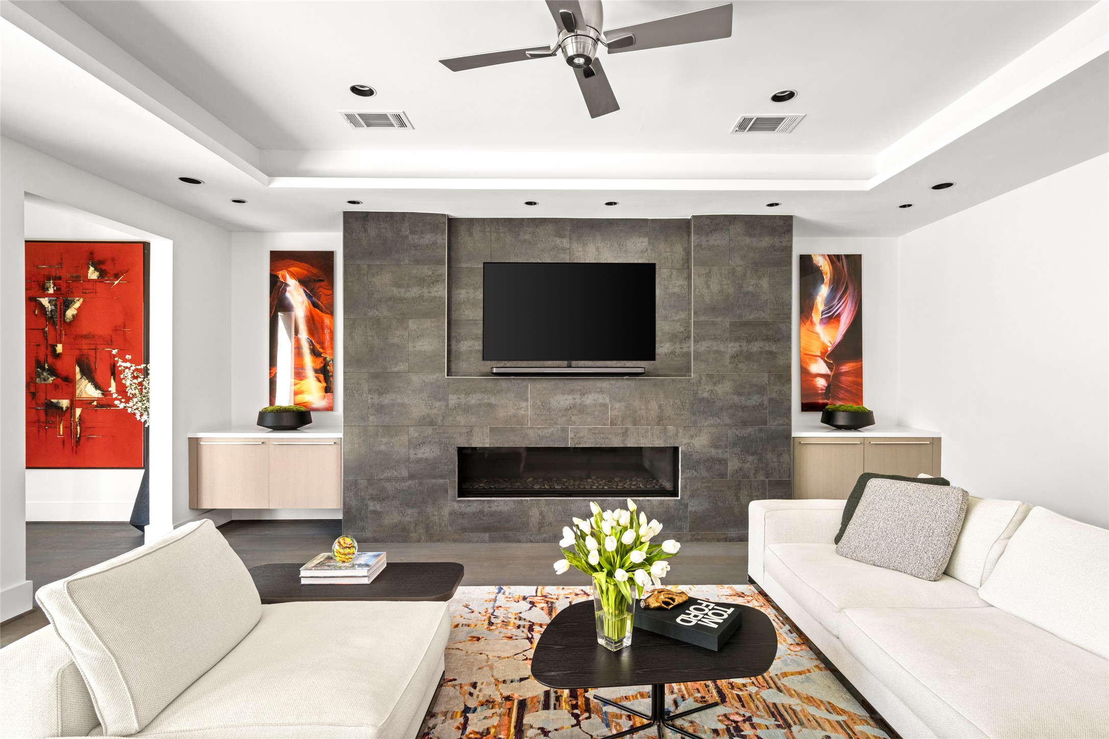 3703 Wroxton Road West University Place, TX 77005 - Photo 14 of 50 Modern living room featuring a sleek, dark-tiled fireplace wall with a mounted TV, flanked by built-in cabinets. The space is bright with natural light and recesses lighting in the ceiling.