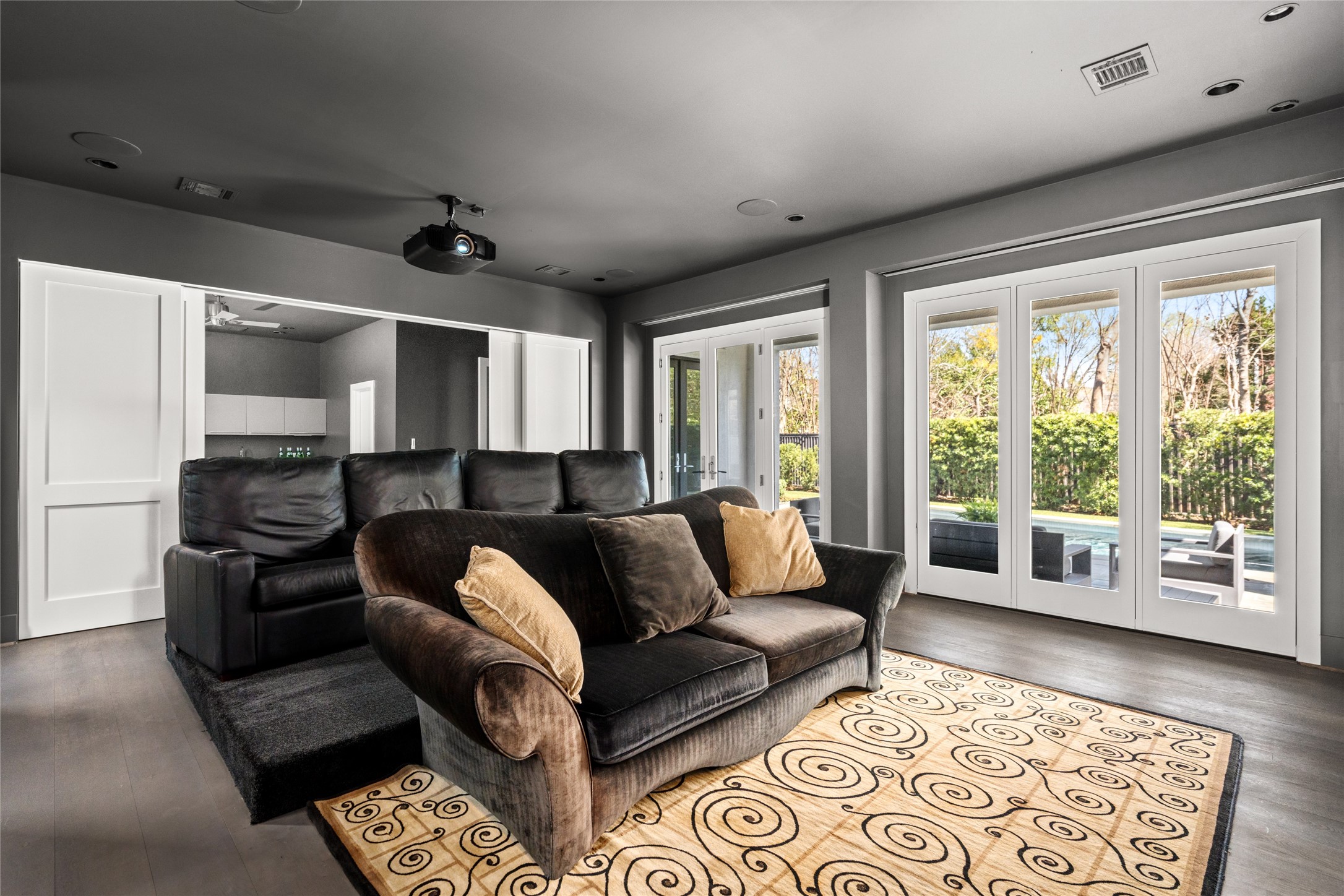 3703 Wroxton Road West University Place, TX 77005 - Photo 24 of 50 This cozy home theater features a ceiling-mounted projector, and large glass doors opening to a lush backyard with a pool, perfect for relaxation and entertainment.