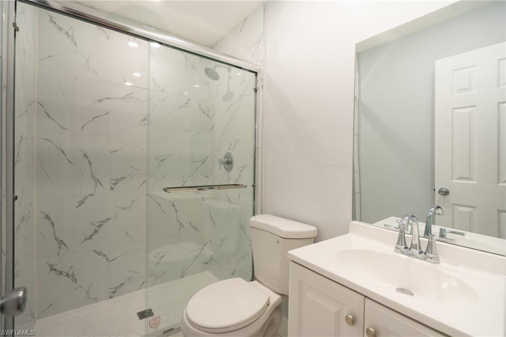 1940 48th Street Southwest Naples, FL 34116 - Photo 31 of 33 Bathroom featuring a glass-enclosed shower with large format marble-look wall tiling, a white vanity with an integrated sink, a chrome faucet, and a rectangular wall mirror
