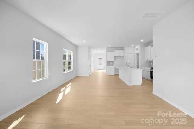 a view of an empty room with kitchen and window