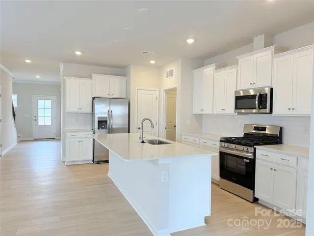 a large kitchen with stainless steel appliances granite countertop a stove a sink a refrigerator and white cabinets with wooden floor