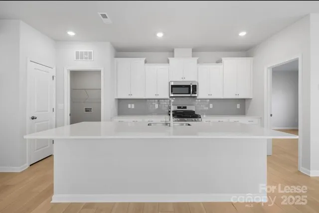 a large white kitchen with kitchen island a sink stainless steel appliances and cabinets