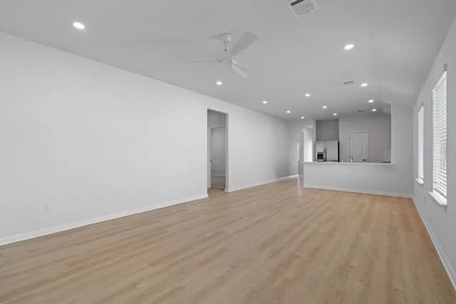 a view of an empty room with wooden floor and a kitchen