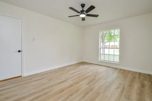 an empty room with wooden floor fan and windows