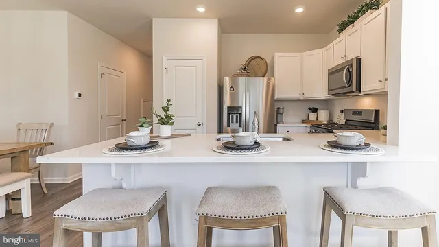 a kitchen with stainless steel appliances kitchen island granite countertop a dining table chairs and a refrigerator