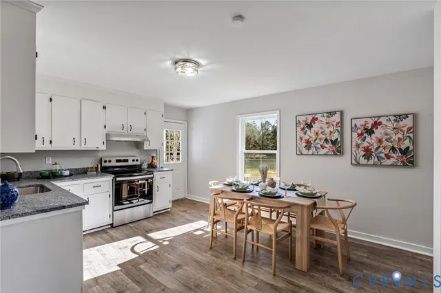 a kitchen with stainless steel appliances granite countertop a stove top oven a sink a dining table and chairs with wooden floor