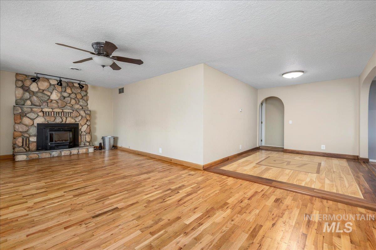 3002 Frozen Dog Road Emmett, ID 83617 - Photo 14 of 50 Unfurnished living room with light wood-type flooring, ceiling fan, a textured ceiling, arched walkways, and a fireplace