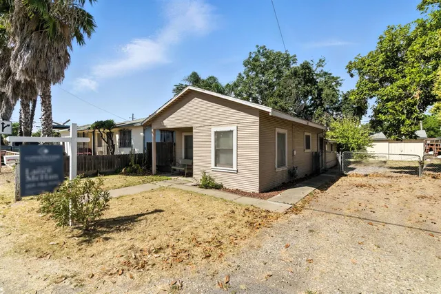 a front view of a house with a dirt yard and a large tree