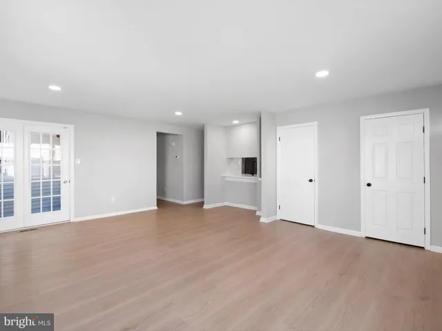 a view of an empty room with wooden floor and a kitchen