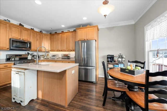 a kitchen with stainless steel appliances granite countertop a refrigerator a stove a sink a dining table and chairs with wooden floor