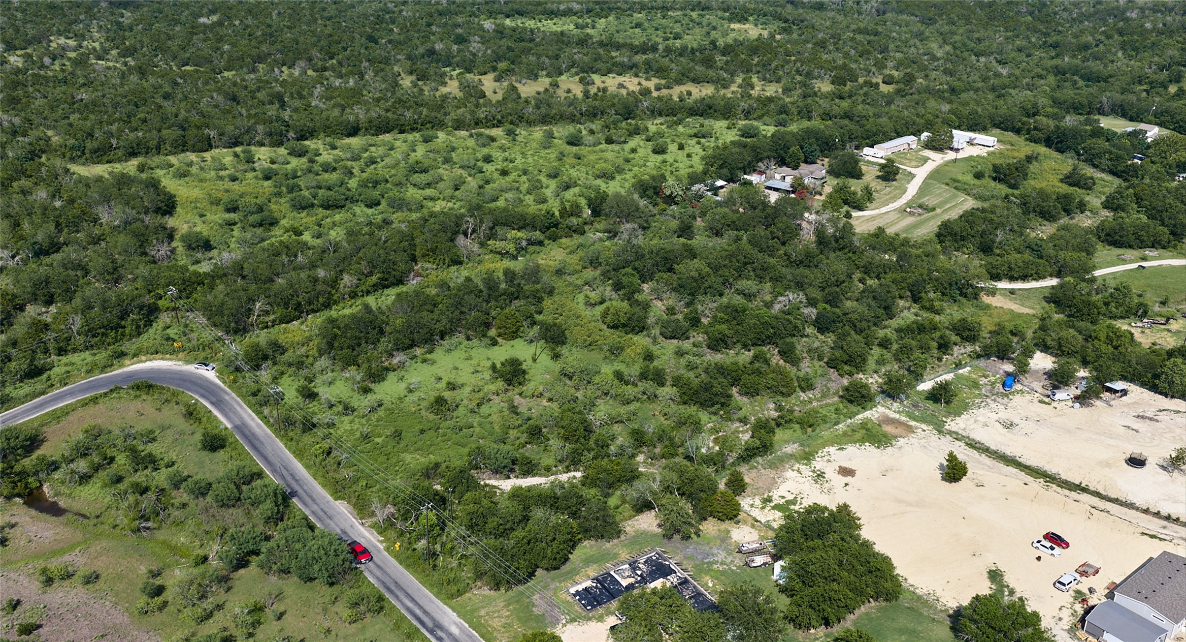 1400 Williamson Road Kyle, TX 78640 - Photo 11 of 13 An aerial panorama reveals verdant, rolling hills with scattered structures, offering a picturesque countryside retreat.