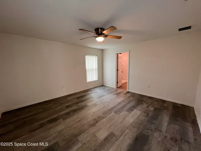 an empty room with wooden floor ceiling fan and window