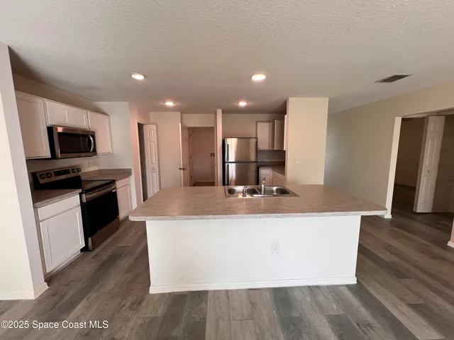 a view of a kitchen with kitchen island a sink wooden floor and stainless steel appliances