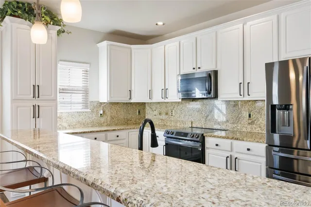 a kitchen with stainless steel appliances granite countertop a refrigerator a sink a stove a dining table and chairs