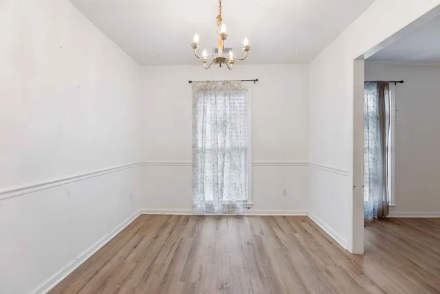 an empty room with wooden floor chandelier and windows