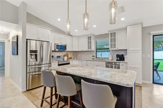 a kitchen with granite countertop stainless steel appliances a refrigerator a stove a sink a dining table and chairs with wooden floor