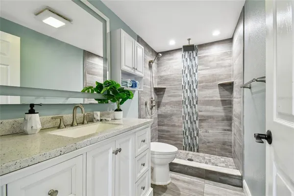 a bathroom with a granite countertop sink a toilet a mirror and shower