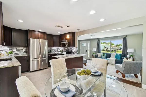 a kitchen with stainless steel appliances kitchen island granite countertop a refrigerator a stove a dining table and chairs with wooden floor