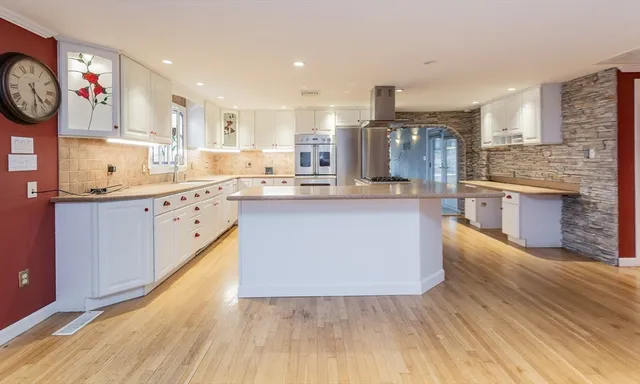 a large kitchen with stainless steel appliances granite countertop a stove top oven a sink dishwasher and a fireplace with wooden floor