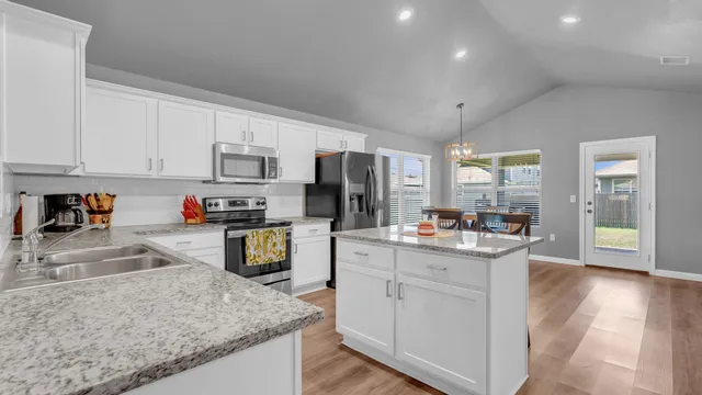 a kitchen with stainless steel appliances granite countertop a stove top oven a sink a refrigerator white cabinets and wooden floor