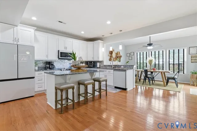 a kitchen with stainless steel appliances granite countertop a refrigerator a stove top oven a sink dishwasher and white cabinets with wooden floor