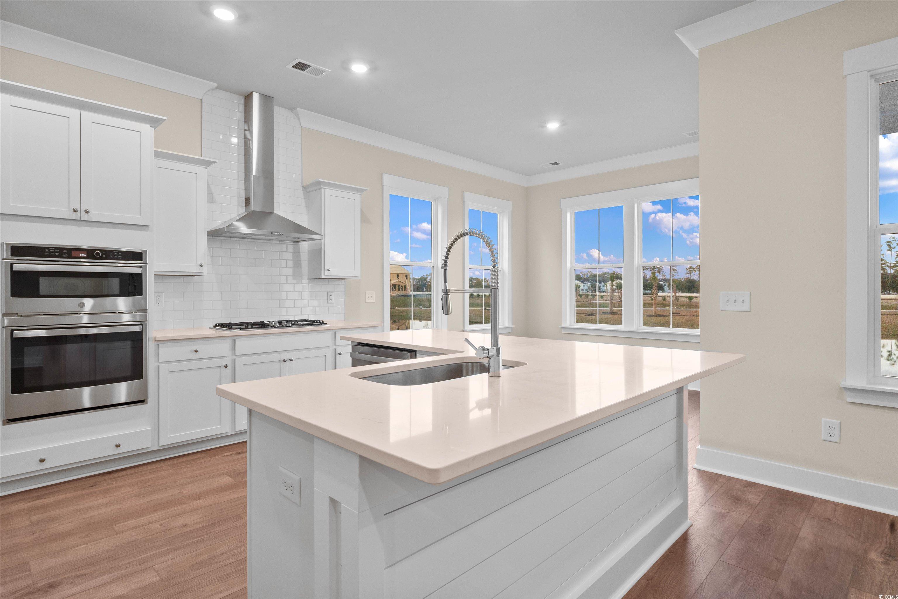 224 Atlantic Breeze Street Myrtle Beach, SC 29572 - Photo 21 of 39 Kitchen with white cabinetry, tasteful backsplash, an island with sink, wall chimney range hood, and double oven