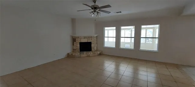 a view of an empty room with chandelier fan and fire place