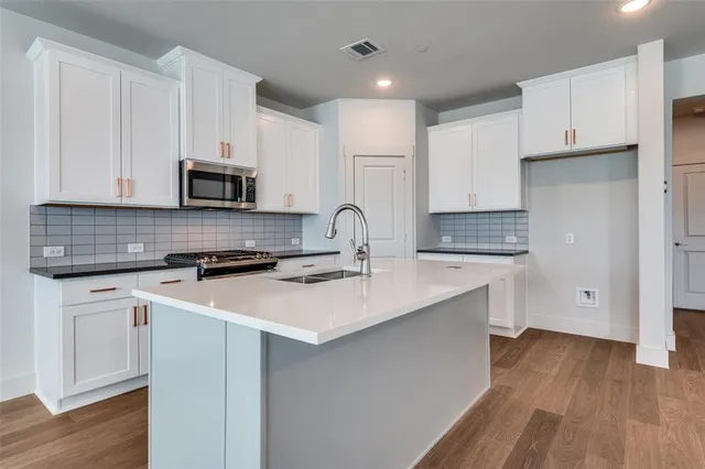 a kitchen with stainless steel appliances a sink dishwasher a stove top oven a refrigerator with white cabinets and wooden floor