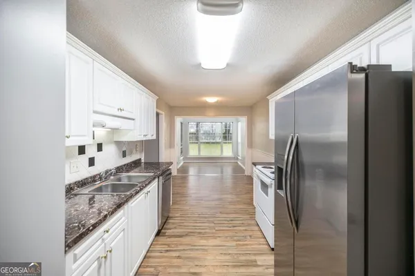 a kitchen with stainless steel appliances granite countertop a refrigerator a sink dishwasher a stove and a dining table with wooden floor