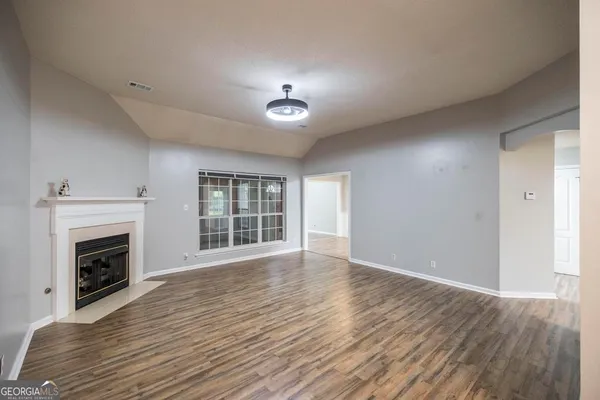 an empty room with wooden floor fireplace and windows