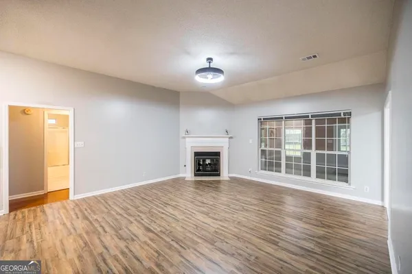 a view of an empty room with wooden floor fireplace and a window
