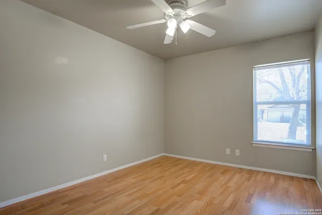 an empty room with wooden floor fan and windows