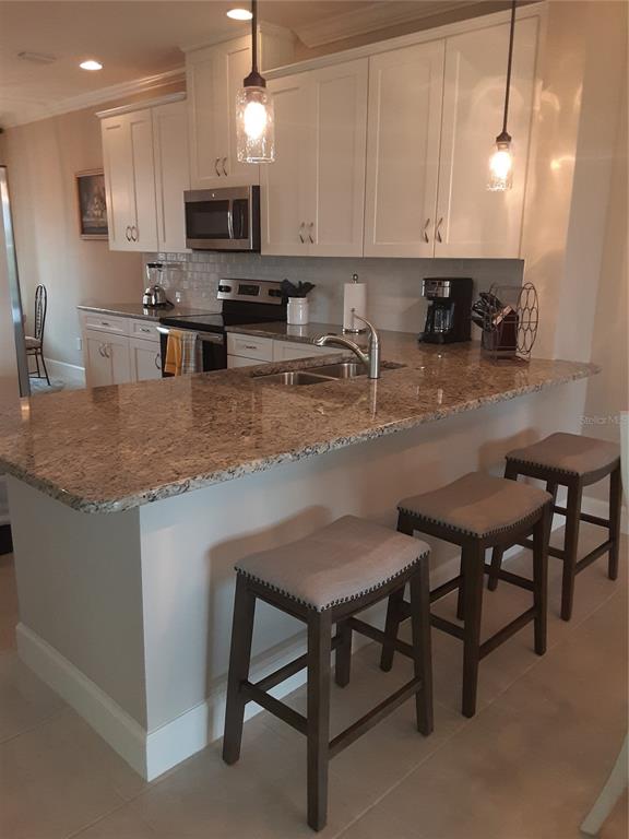 13605 Messina Loop, Unit 104 Bradenton, FL 34211 - Photo 9 of 38 a kitchen with kitchen island granite countertop a stove a sink a microwave and a refrigerator