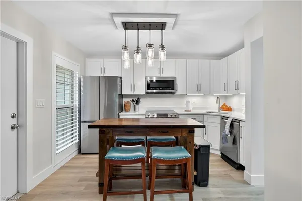a kitchen with stainless steel appliances a dining table chairs microwave and refrigerator
