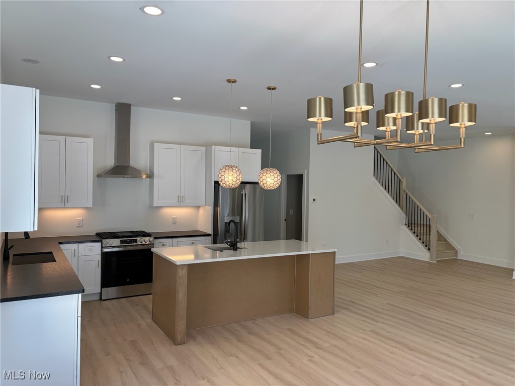 Kitchen featuring pendant lighting, white cabinets, appliances with stainless steel finishes, a kitchen island, and wall chimney range hood